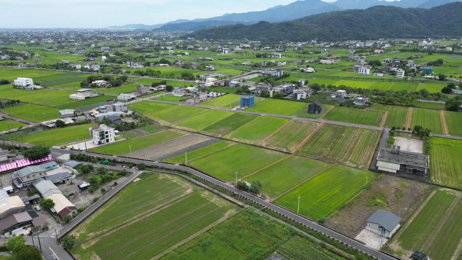 空拍山腳下大片綠色農田、田間道路與零散的透天住宅